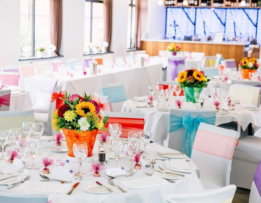 Decorated wedding reception tables with colourful floral centrepieces and glassware at Roffey Park Venue
